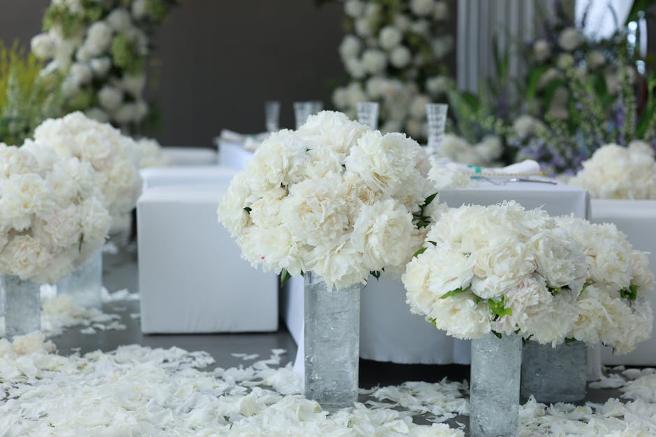 A floral arrangement featuring large, fluffy white hydrangeas and peonies placed in rectangular metallic vases on a table with a white tablecloth. The flowers are fresh with soft, textured petals and 