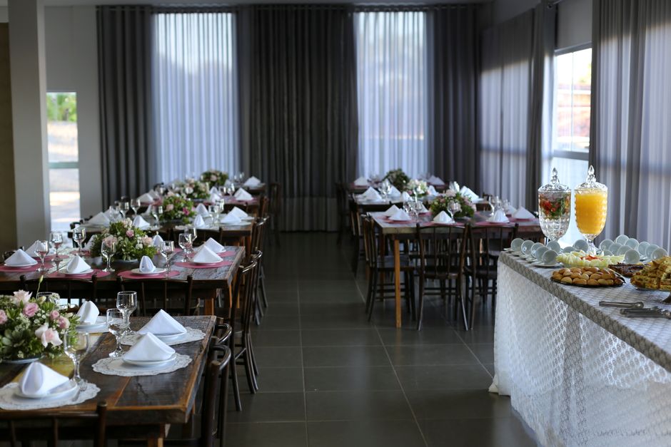 A spacious dining room set up for a formal event with multiple rectangular wooden tables arranged in parallel, each adorned with elegant floral centerpieces comprising pink and white roses, green foli