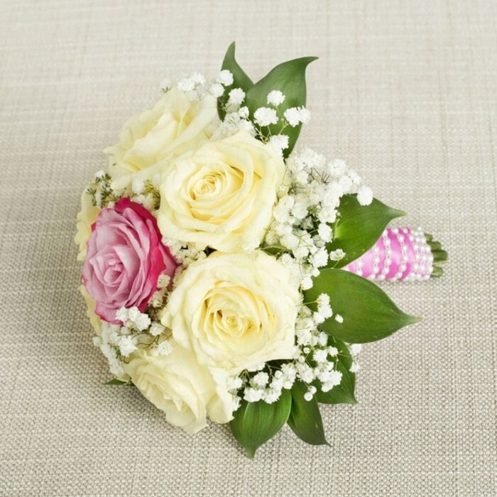 Captured in soft, natural light atop a textured linen canvas-reminiscent of the relaxed charm found along Wandsworth Bridge Road in Sands End-this bouquet offers a visual symphony of creamy roses and a standout magenta bloom. The central focus, five to six large cream-colored roses with petals still tenderly unfurling, imparts a sense of freshness as if picked from a morning garden after gentle rain. Positioned just off-center, a vivid, fuchsia-pink rose commands attention, boldly contrasting the softness surrounding it and providing a radiant highlight amidst the pale palette. Dotted liberally throughout, airy clusters of white gypsophila baby's breath create a dreamy, almost ethereal quality, casting tiny, gentle shadows across the surrounding linen and adding a sense of lightness and grace. The edges are bordered with deep, glossy leaves, their rich green color and subtle sheen framing the entire composition in natural elegance. At the base, the bouquet's stems are firmly and neatly wrapped in a bright, sleek pink satin ribbon, adding a pop of contemporary style, with bands of luminous white pearls spiraling around for a traditional, bridal touch. The arrangement, meticulously crafted by a skilled florist, evokes the essence of wedding celebrations in Sands End-where modern flair meets timeless romance, and every petal reflects local artistry. This bouquet is ideal for bridesmaids or intimate ceremonies, encapsulating both beauty and the emotional resonance of a memorable event in this vibrant London neighborhood.