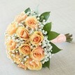 Embracing romantic simplicity, this hand-tied bouquet embodies the spirit of special celebrations across Sands End. Gathered tightly, peach and apricot-toned roses unfurl in soft spirals, their petals luminous and inviting, shifting harmoniously from pale peach at the edges towards a richer apricot core. Fine clouds of white gypsophila wrap around the roses, as delicate as lace and just as timeless-a gentle nod to bridal veils seen at local ceremonies along Wandsworth Bridge Road. Lush, glossy green leaves peek out between the blooms, providing vibrant depth and suggesting the renewal so often celebrated in local riverside parks. The bouquet's stems are bundled neatly and encased in an elegant peach-hued ribbon, carefully adorned with a row of tiny white pearls in a subtle, sophisticated pattern-offering a tactile finish to the hand. Under the gentle light flowing in from a window, each rose and leaf shimmers with freshness, the whole arrangement quietly signalling hope, joy, and the love stories woven through Sands End. The bouquet's gentle scent-a whisper of roses with an undercurrent of green-adds to its allure, making it a perfect companion for a bride, or a meaningful gift to mark anniversary moments or joyful beginnings.